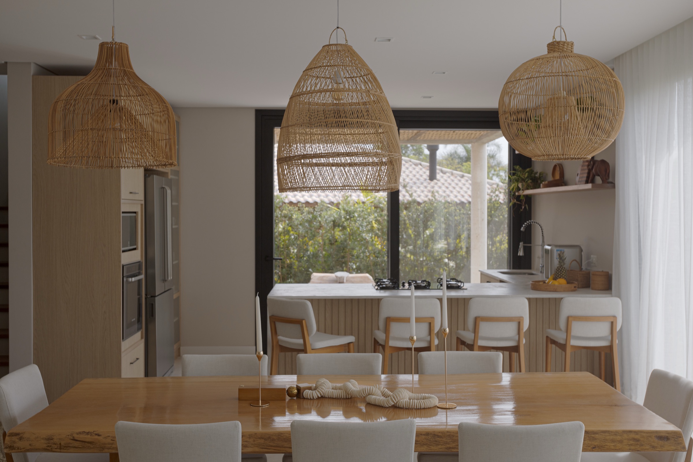 Mesa de jantar sob luminárias de fibra natural, com a cozinha ao fundo